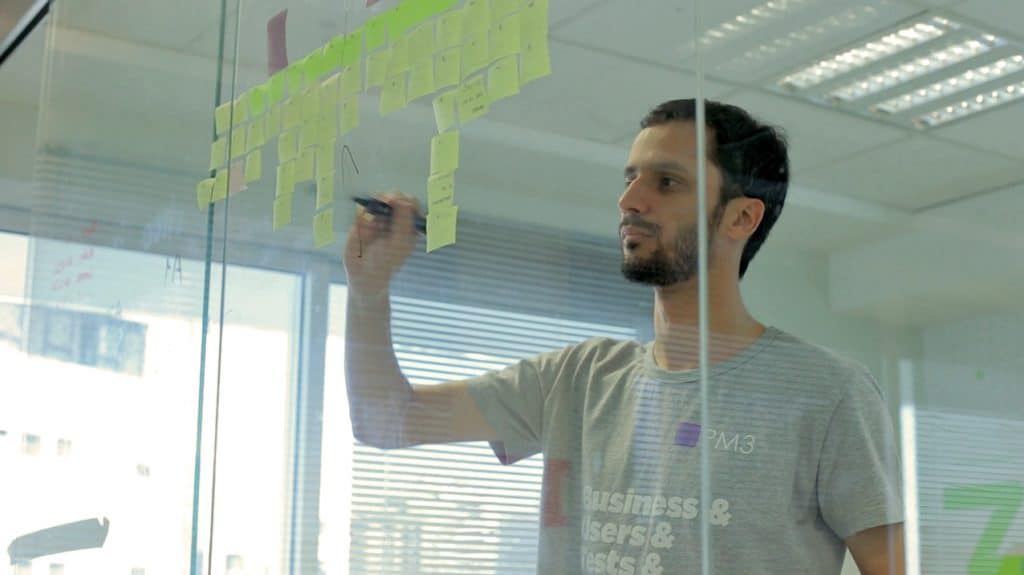 A imagem mostra Raphael Farinazzo, Product Manager na Xerpa, escrevendo em um quadro com post-its.